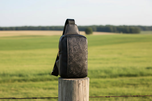 Black leather sling bag with gold accents on a white background